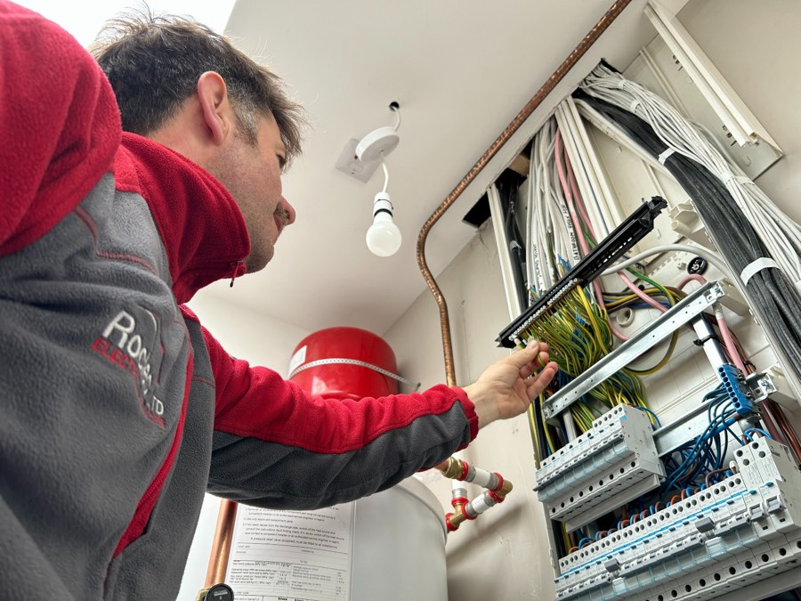 Roy O'Connor, Owner of Roclec Electrical Services, working on a residential distribution board in a red Roclec hoodie.